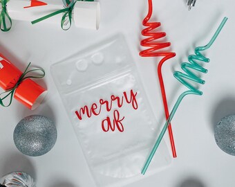May include: A clear plastic bag with the words "merry af" written in red on it. The bag is surrounded by silver ornaments and two colorful bendy straws.