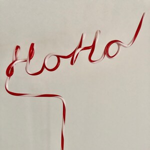 May include: A red and white striped plastic straw bent into the word "hello".