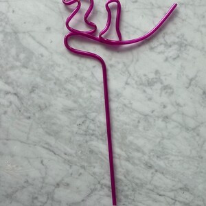 May include: A purple plastic drinking straw bent into a decorative shape.