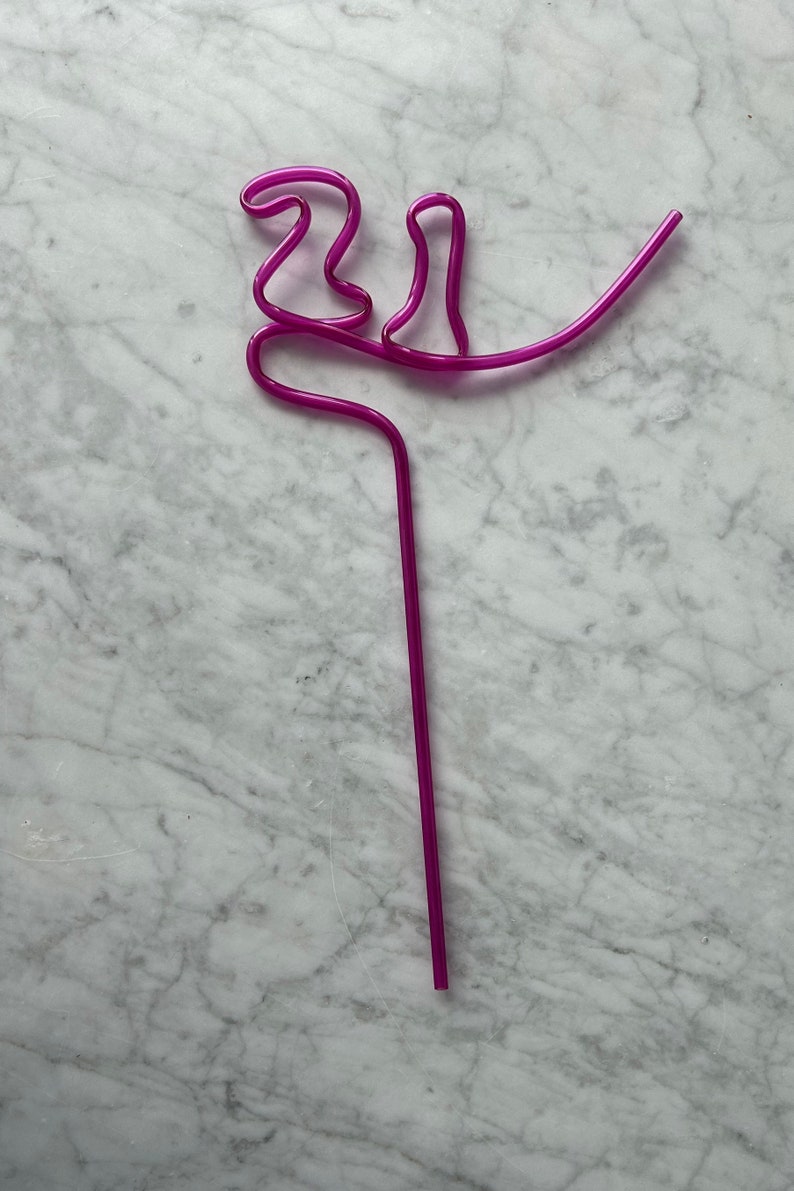 May include: A purple plastic drinking straw bent into a decorative shape.