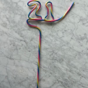 May include: A colorful, striped drinking straw bent into the shape of the number 21. The straw is pink, blue, and yellow.