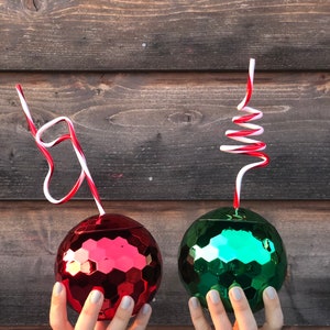 May include: Two disco ball-shaped cups with red and green mirrored surfaces. Each cup has a red and white striped straw.