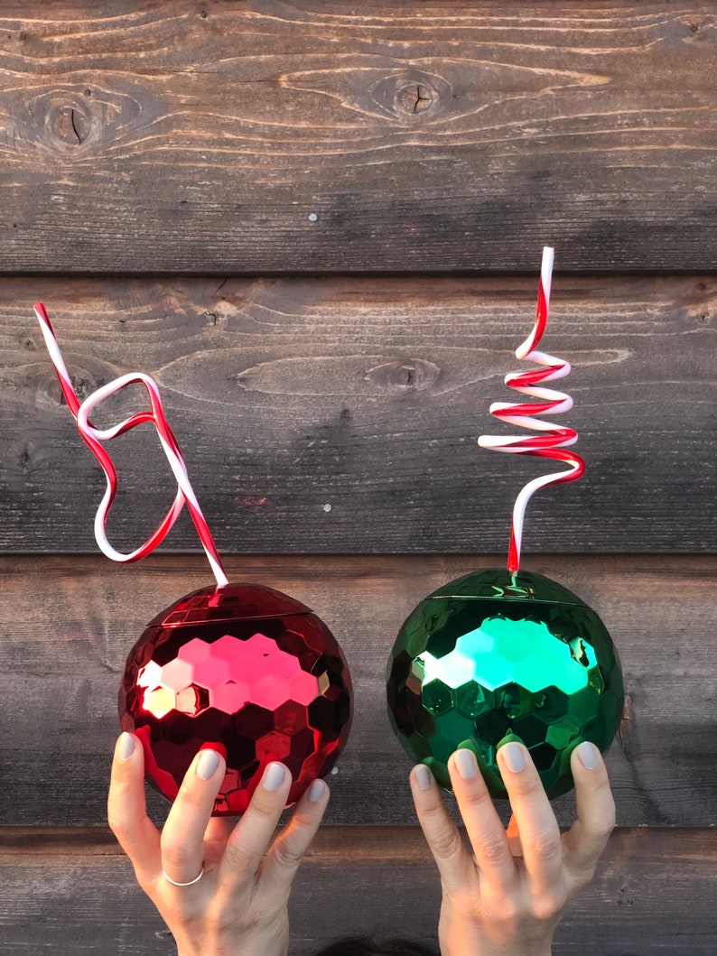 May include: Two disco ball-shaped cups with red and green mirrored surfaces. Each cup has a red and white striped straw.