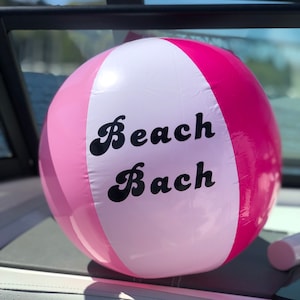 May include: A pink and white beach ball with the words "Beach Bach" printed in black.