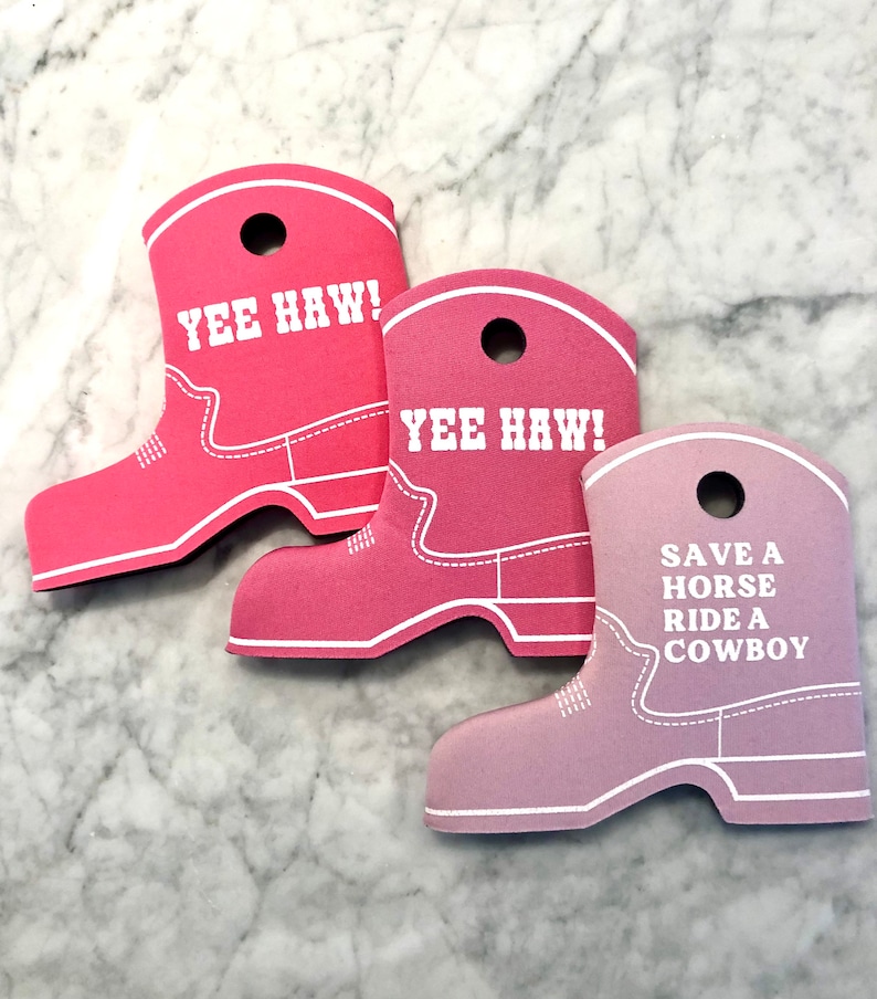 K&ouml;nnte beinhalten: Drei rosa Cowboy-Stiefel aus Schaumstoff als Dekoration. Die beiden oberen haben den Text "Yee Haw!" aufgedruckt. Die untere Dekoration hat den Text "Save a horse, ride a cowboy" aufgedruckt.