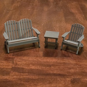 May include: A miniature gray Adirondack-style outdoor furniture set. The set includes a double bench, a single chair, and a small side table. The furniture is made of wood and has a classic slatted design. Perfect for a dollhouse or miniature garden.