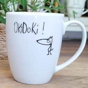 Puede incluir: Taza de cerámica blanca con una ilustración en blanco y negro de un perro y el texto "OkiDoki!" impreso en el lateral.