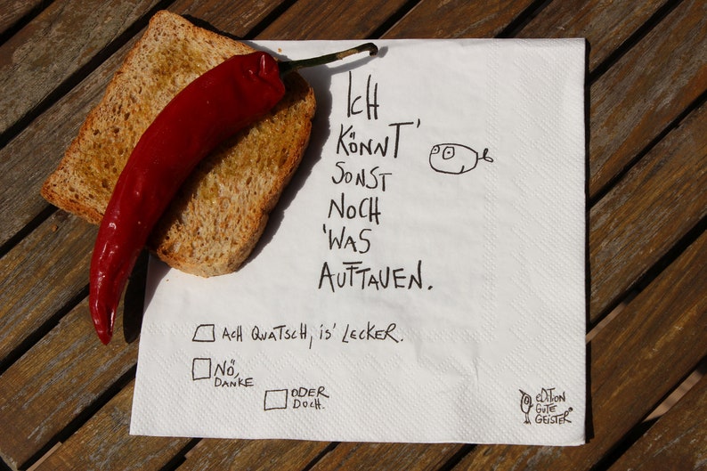 May include: A white napkin with black handwritten text that reads "Ich Konnt' Sonst Noch 'Was Auftauen. Ach Quatsch, is' Lecker. No Danke Oder Doch." There is a red chili pepper and a piece of toasted bread on the napkin.