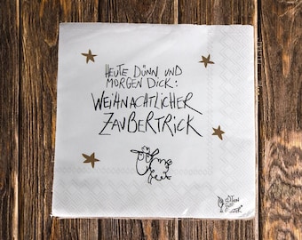 Könnte beinhalten: Eine quadratische weiße Papierserviette mit goldenen Sternen und schwarzem handgeschriebenem Text: Heute dünn und morgen dick: weihnachtlicher Zaubertrick. Unter dem Text befindet sich eine kleine schwarze Strichzeichnung eines Schafes.