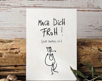 May include: A white card with the handwritten phrase "MACH DICH FROH!" and a simple illustration of a figure. The card is propped up on a wooden surface, with olives and stones in the foreground.