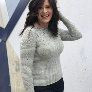 May include: A light gray sweater with a blue speckled pattern. The sweater has long sleeves and a round neckline.