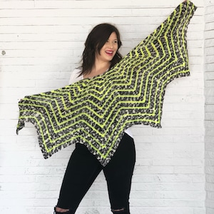 May include: A black and neon green crochet shawl with a chevron pattern. The shawl is draped over a person's shoulders.