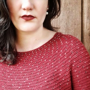 May include: A close-up of a woman wearing a red sweater with white polka dots. The sweater has a scoop neck and is made of a soft, textured fabric.