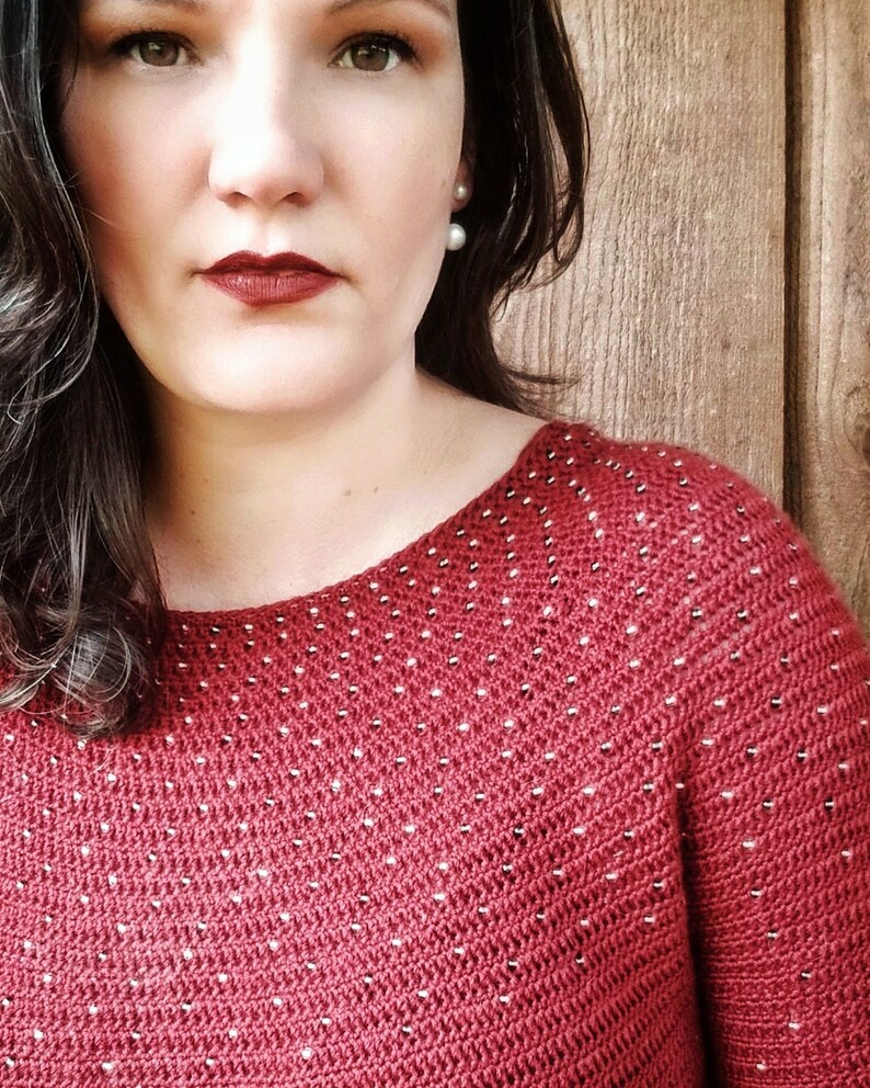 May include: A close-up of a woman wearing a red sweater with white polka dots. The sweater has a scoop neck and is made of a soft, textured fabric.