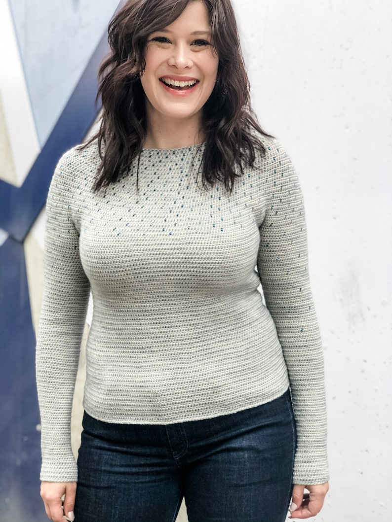 May include: A light gray sweater with a textured pattern and a subtle blue speckling throughout. The sweater has long sleeves and a round neckline.