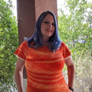 May include: A woman wearing a crocheted top with orange and white stripes. The top has a scoop neck and short sleeves.
