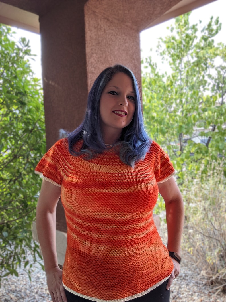 May include: A woman wearing a crocheted top with orange and white stripes. The top has a scoop neck and short sleeves.