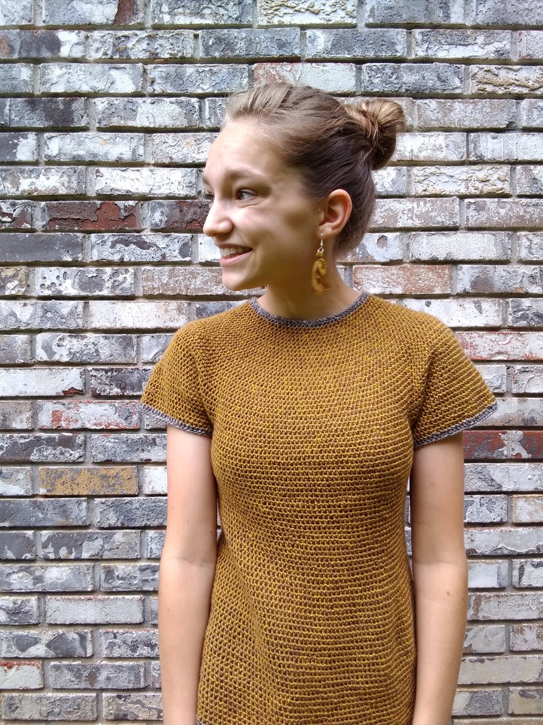 May include: A woman wearing a mustard yellow crochet top with short sleeves and a grey trim. The top has a textured, open-stitch design.