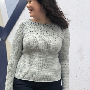 May include: A light gray crochet sweater with a blue speckled pattern. The sweater has long sleeves and a round neckline.