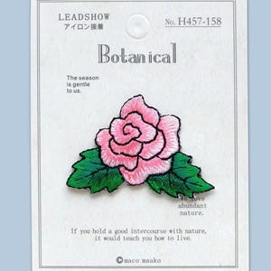 May include: Embroidered patch of a pink rose with green leaves, labelled "Botanical." The patch is on a white card with Japanese text and the phrase "The season is gentle to us."