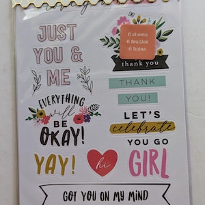 May include: A sheet of stickers with a floral theme. The stickers feature phrases like "Just You & Me", "Everything Will Be Okay", "Let's Celebrate", and "You Go Girl".