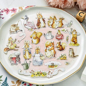 May include: A collection of colorful animal stickers featuring squirrels, rabbits, and a hedgehog. The stickers are on a white plate with a gold rim.