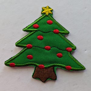 Könnte beinhalten: Ein grüner Filz-Weihnachtsbaum mit roten Kugeln und einem gelben Stern oben. Der Baum hat einen braunen Filzstamm.