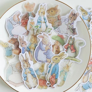 Peut inclure: Une feuille d'autocollants colorés illustrant Peter Rabbit et d'autres personnages des livres pour enfants de Beatrix Potter. Les autocollants sont parfaits pour ajouter une touche de fantaisie aux journaux, aux planificateurs et à d'autres projets d'artisanat.