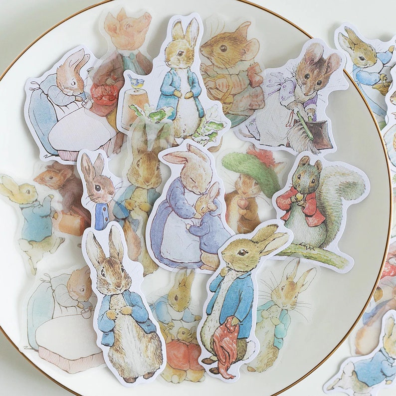 May include: A sheet of colorful stickers featuring illustrations of Peter Rabbit and other characters from Beatrix Potter's children's books. The stickers are perfect for adding a touch of whimsy to journals, planners, and other craft projects.