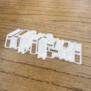 May include: A white metal die cut of a stack of books. The die cut is designed to be used for scrapbooking, card making, and other paper crafts.