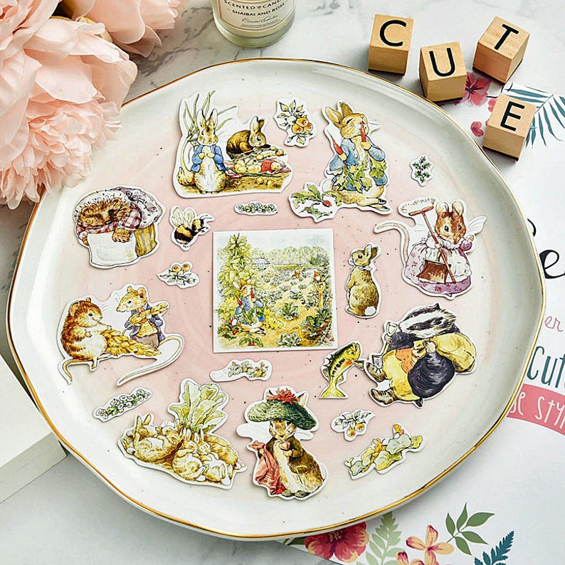 May include: A set of 15 colorful stickers featuring illustrations of Peter Rabbit characters. The stickers are on a pink background and include Peter Rabbit, Benjamin Bunny, and other characters from the book.