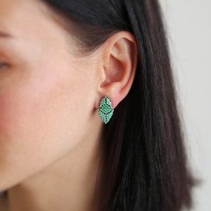 May include: A pair of green leaf-shaped earrings. The earrings are made of small beads and are a delicate and feminine accessory.