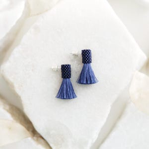 May include: A pair of blue beaded tassel earrings with silver posts. The tassels are made of a soft, blue fabric and are about 1 inch long.