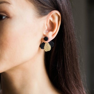 Puede incluir: Un par de pendientes de cuentas negras y doradas con un diseño geométrico. Los pendientes están hechos de cuentas pequeñas y tienen una forma de abanico colgante.