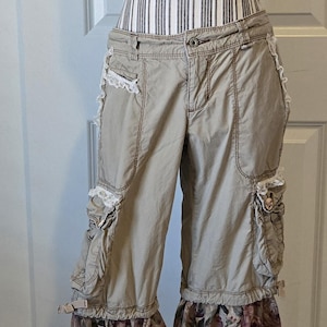 以下が含まれることがあります： フローラルプリントのベルボトムが付いたタンカーゴパンツ。パンツには複数のポケット、レーストリム、ボタン留めが付いています。ベルボトムは、バーガンディ、グリーン、クリーム色のダークフローラルパターンが特徴です。パンツはマネキンに表示されています。