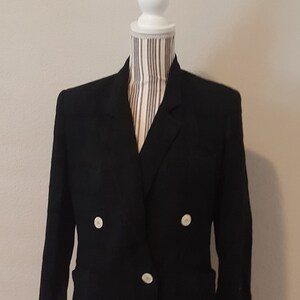 May include: A black double-breasted blazer with three white buttons on each side. The blazer is displayed on a white mannequin with a striped fabric neck. The sleeves are three-quarter length.