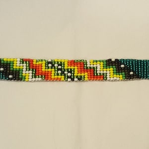 May include: A beaded bracelet with a green, white, yellow, red, and black geometric pattern. The bracelet has silver metal clasps.
