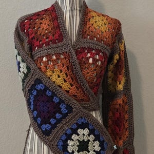 May include: A long-sleeve wrap cardigan constructed from multi-colored granny square crochet patches. The garment features a brown yarn border connecting squares in shades of red, orange, yellow, blue, purple, and cream, with a V-neckline.