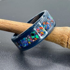 May include: A dark blue ring with a silver band and a colorful inlay of iridescent opal chips.