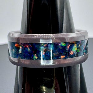 May include: A black tungsten carbide ring with a band of iridescent blue, green, and orange opal inlay.