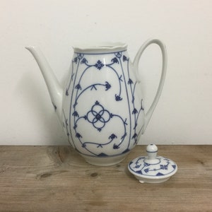 May include: A white porcelain coffee pot with a blue and white floral pattern. The pot has a rounded body and a spout on the side. The lid is separate and has a knob on top.
