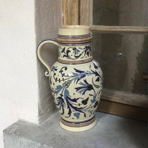 May include: A white ceramic jug with a blue and black floral design. The jug has a handle and a wide mouth.