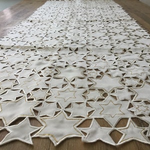 May include: White table runner with a gold star pattern. The stars are cut out of the fabric, creating a delicate and elegant design.