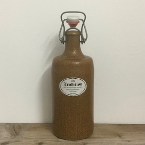 Peut inclure: Une bouteille en céramique brune avec un bouchon à bascule en métal. La bouteille porte une étiquette blanche avec le texte "alte Tradition" et une description en allemand.