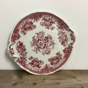 May include: A large, white ceramic serving platter with a scalloped edge and two handles. The platter is decorated with a red floral pattern and a small bird.