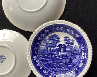 May include: Three white ceramic saucers with blue and white floral patterns. The center saucer features a blue and white landscape scene with a bridge and trees. The back of the saucers have the words "Spode" and "England" printed in blue.