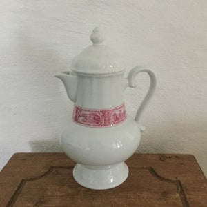 Könnte beinhalten: Weiße Kaffeekanne aus Keramik mit einem rosafarbenen Blumendesign um die Mitte. Die Kanne hat einen Deckel und einen Griff.