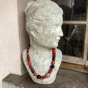 Könnte beinhalten: Eine Halskette aus orangefarbenen und schwarzen Perlen. Die Halskette befindet sich auf einem Gipsabdruck eines Frauenkopfes.