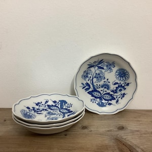 Könnte beinhalten: Eine Sammlung weißer Keramikgeschirr mit blauem Blumenmuster. Das Set umfasst drei kleine, ovale Schalen und einen größeren, runden Teller. Das blaue Design zeigt Blumen und Blätter.