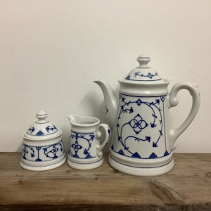 May include: A white porcelain tea set with blue floral designs. The set includes a teapot, creamer, and sugar bowl.